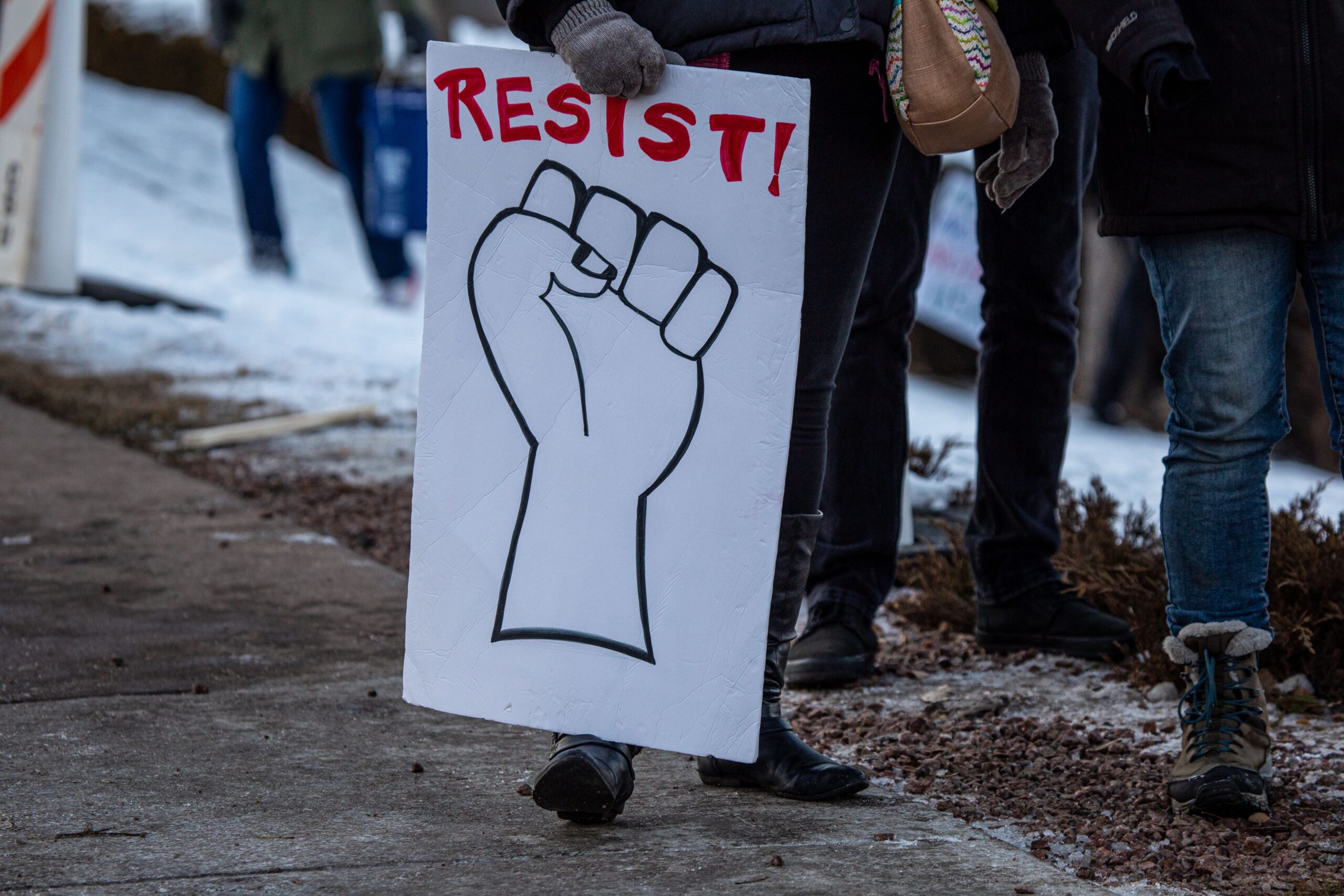 Close-up of a protester holding a sign with a raised fist illustration and the word “RESIST!” written in red during a public demonstration.