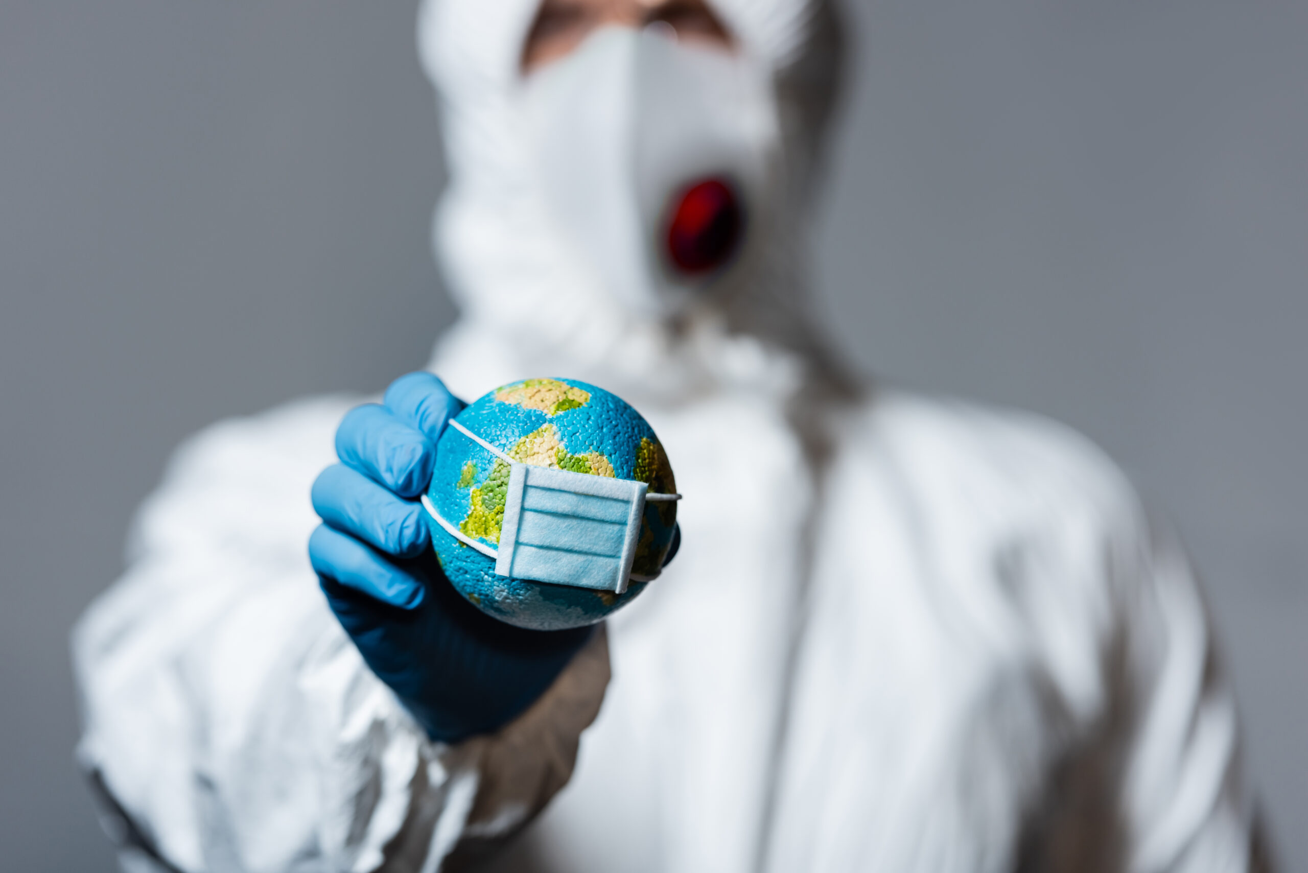 Person wearing a hazmat suit and face mask holding a small globe, symbolizing global health, environmental crisis, or pandemic concerns.