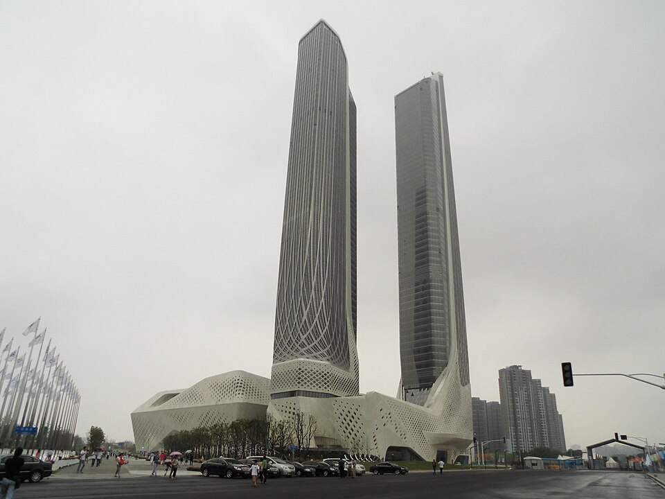 View of the Nanjing International Youth Cultural Centre in China, featuring two modern skyscrapers designed by architect Zaha Hadid against a cloudy sky.