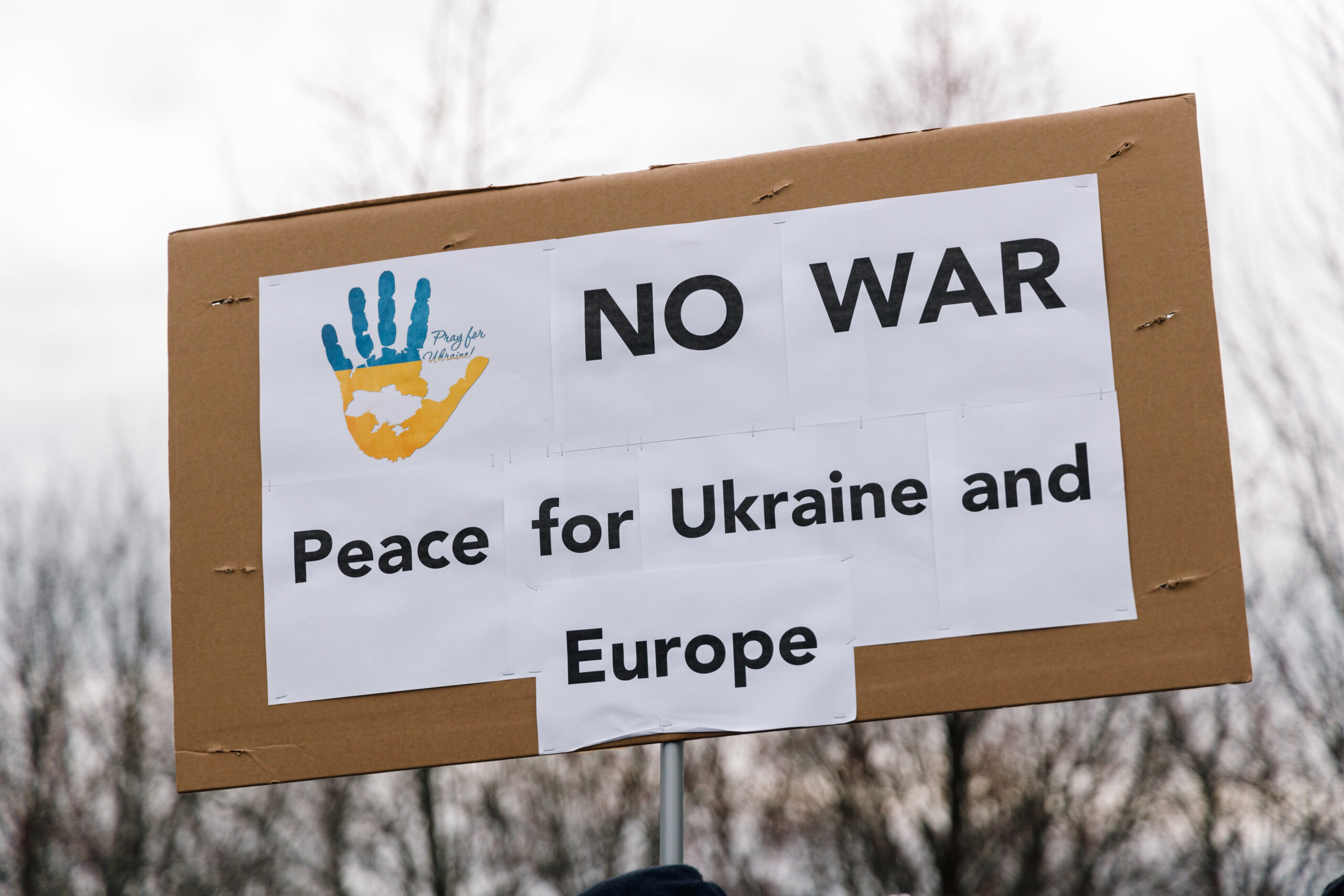 Protest sign reading “NO WAR” and “Peace for Ukraine and Europe,” featuring a blue and yellow handprint symbol.