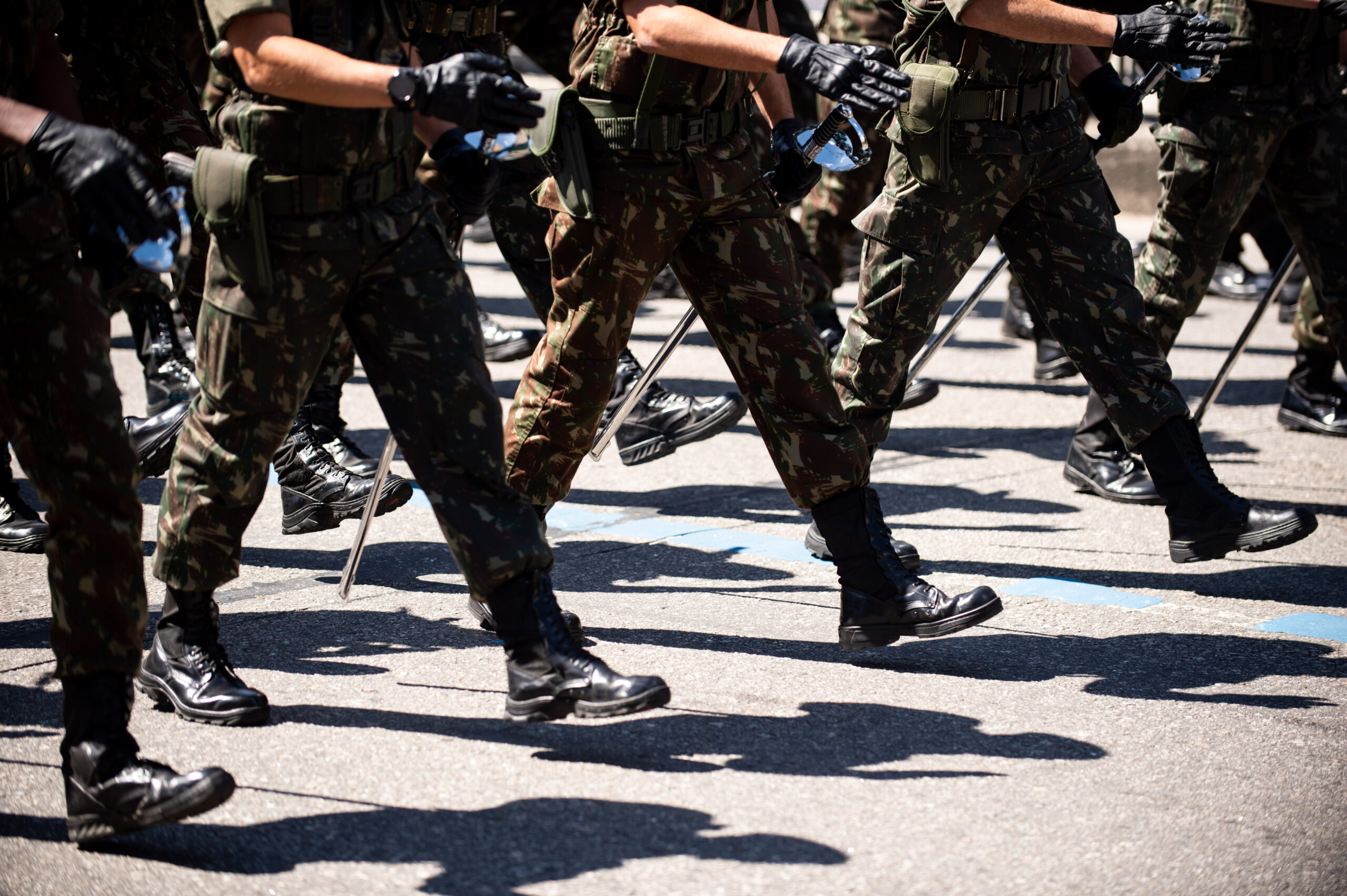 Close-up view of soldiers marching in formation during a military parade, wearing camouflage uniforms, black boots, and carrying batons.
