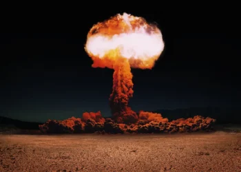 Dramatic image of a massive nuclear explosion forming a bright mushroom cloud rising into the night sky above a barren landscape.