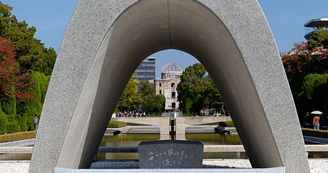 View of the Hiroshima Memorial Cenotaph in Hiroshima Peace Memorial Park, framing the Eternal Flame and memorial structures in the distance.