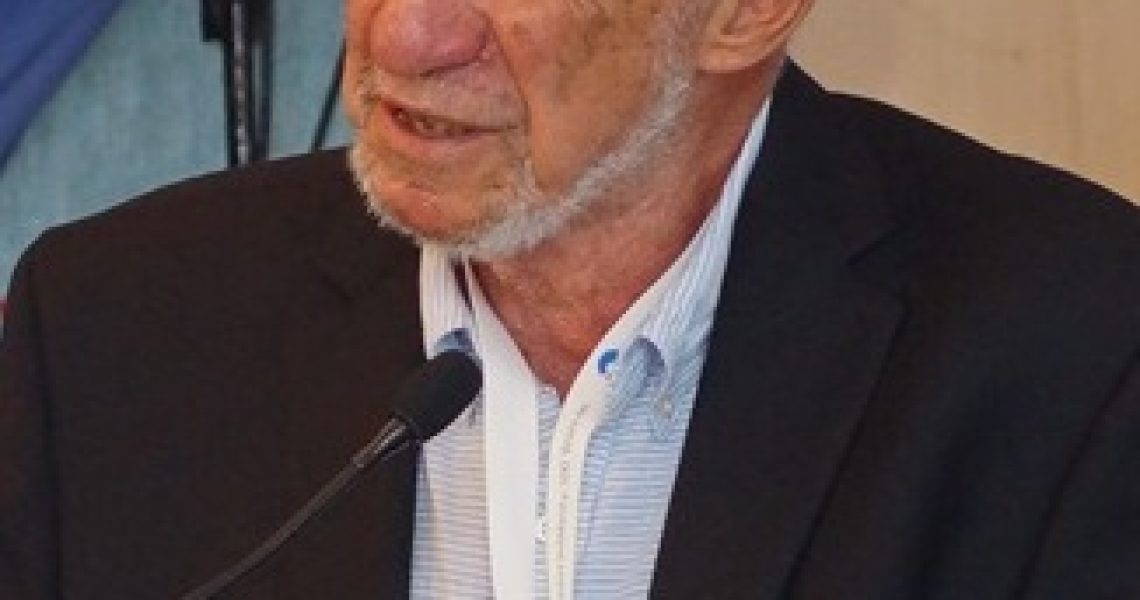 Richard A. Falk speaking at a public event or conference while standing at a microphone.
