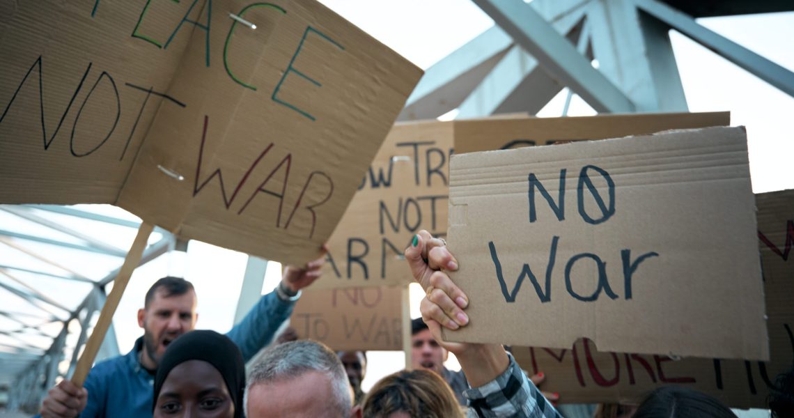 Group of people holding handmade signs reading “No War” and “Peace Not War” during a protest