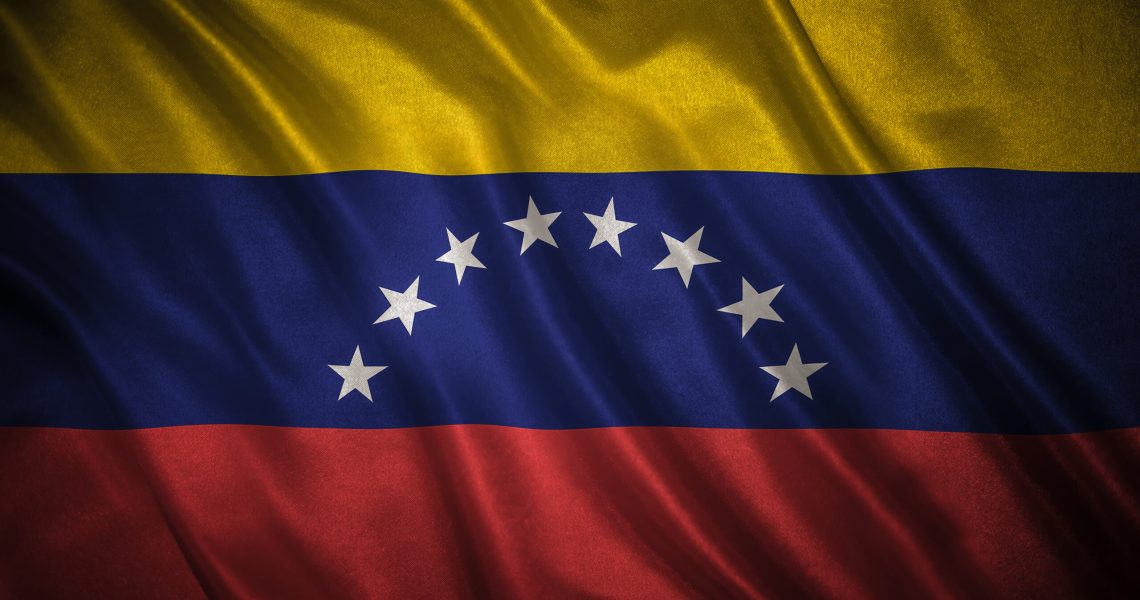 Flag of Venezuela waving in the wind, showing the yellow, blue, and red stripes with white stars across the center.