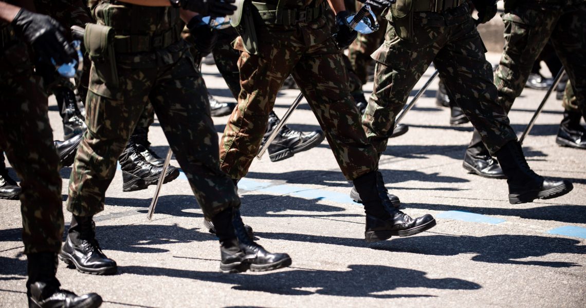 Close-up view of soldiers marching in formation during a military parade, wearing camouflage uniforms, black boots, and carrying batons.