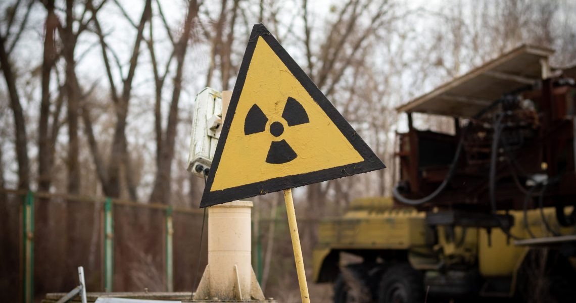 Old yellow radiation sign against a blurred background of equipment that participated in the liquidation of the accident consequences in Chernobyl Exclusion Zone, Ukraine