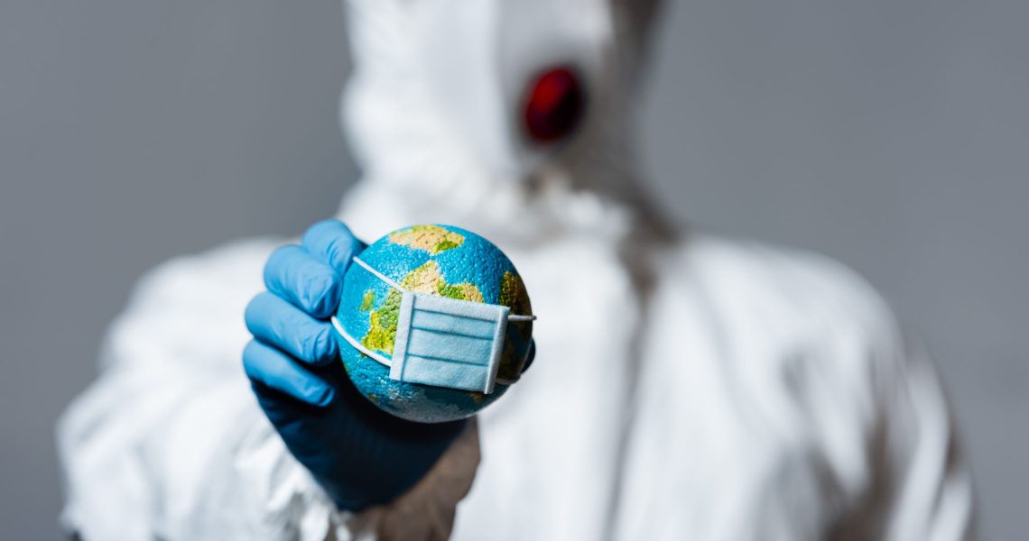 Person wearing a hazmat suit and face mask holding a small globe, symbolizing global health, environmental crisis, or pandemic concerns.