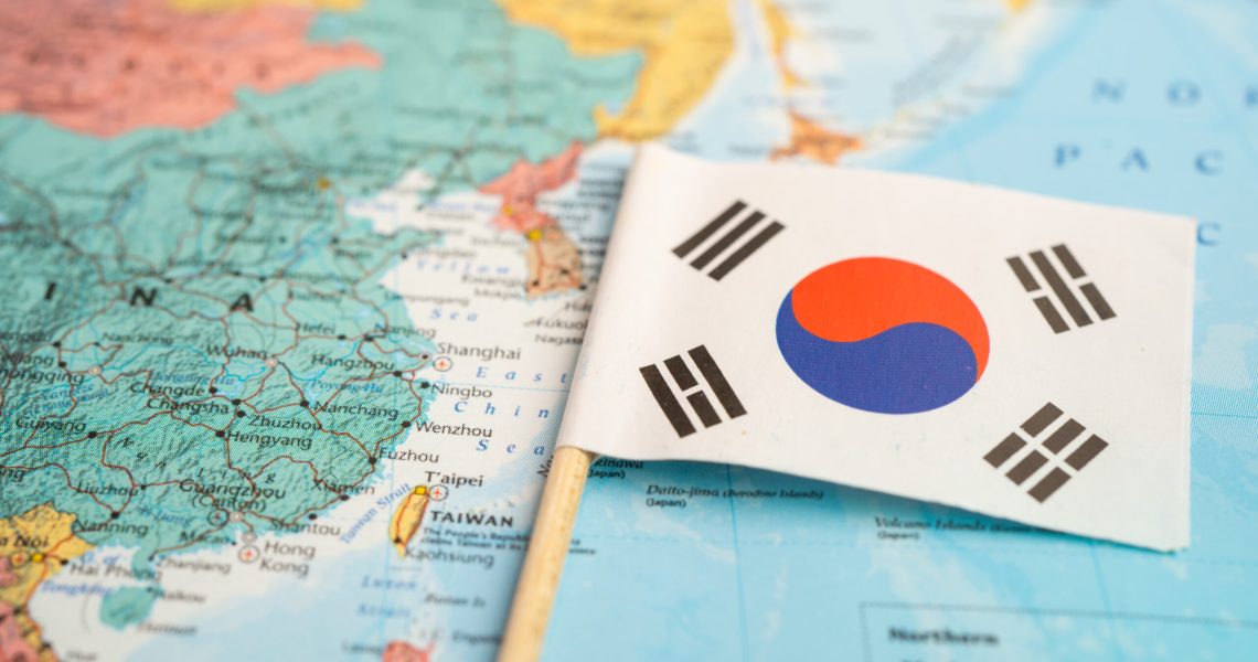 Small South Korea flag placed on a map of East Asia, with surrounding countries and regional geography visible in the background.