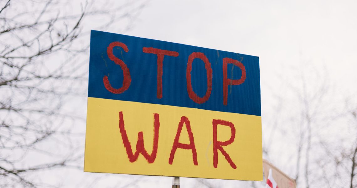 Handmade protest sign reading “STOP WAR” in red letters over blue and yellow colors associated with the Ukrainian flag.